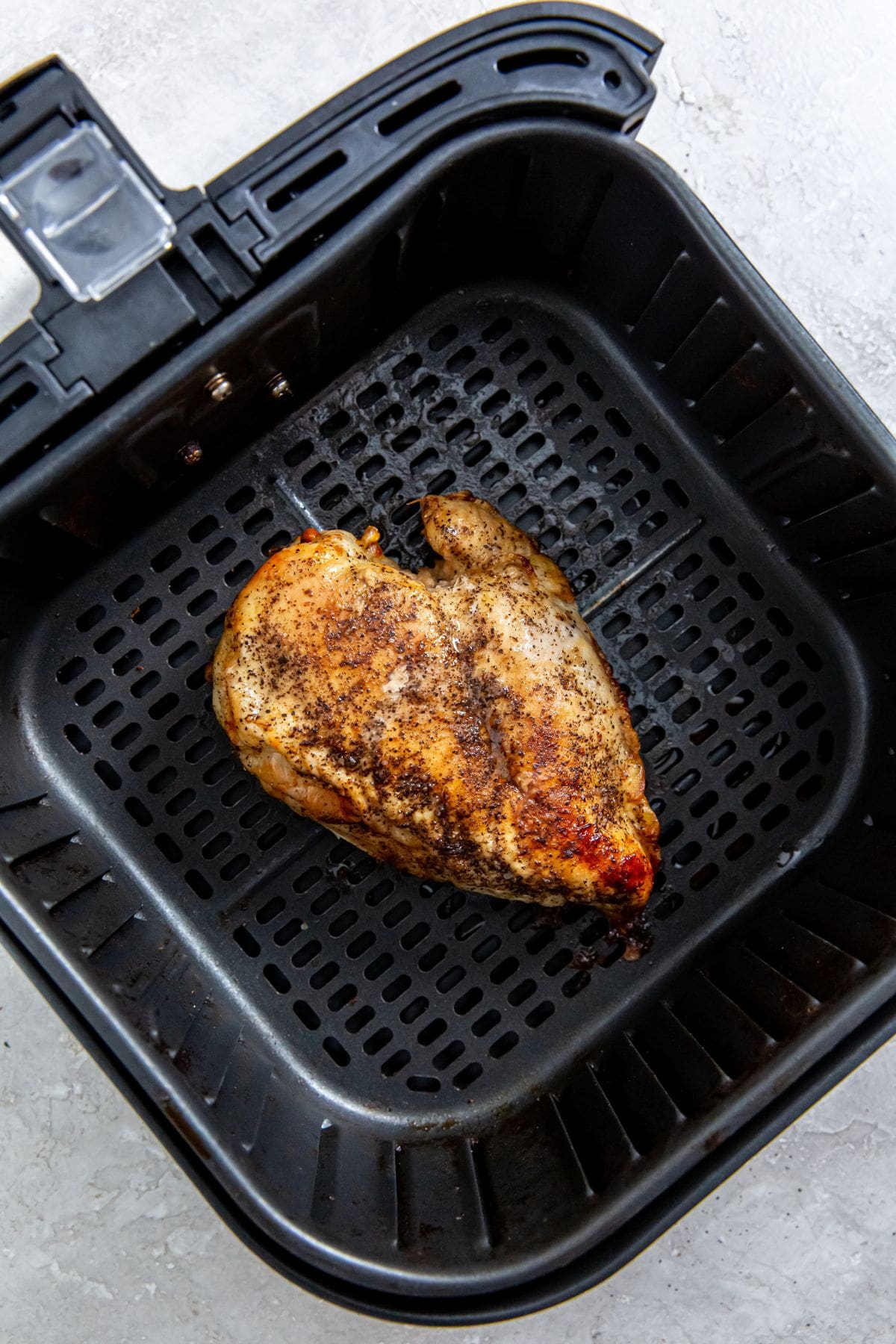 black air fryer with cooked chicken inside