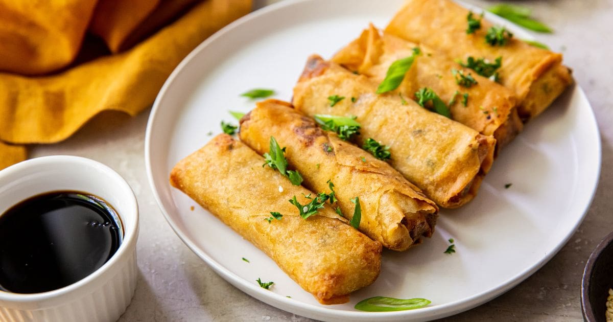 white plate with spring rolls on it. orange bowl next to it.