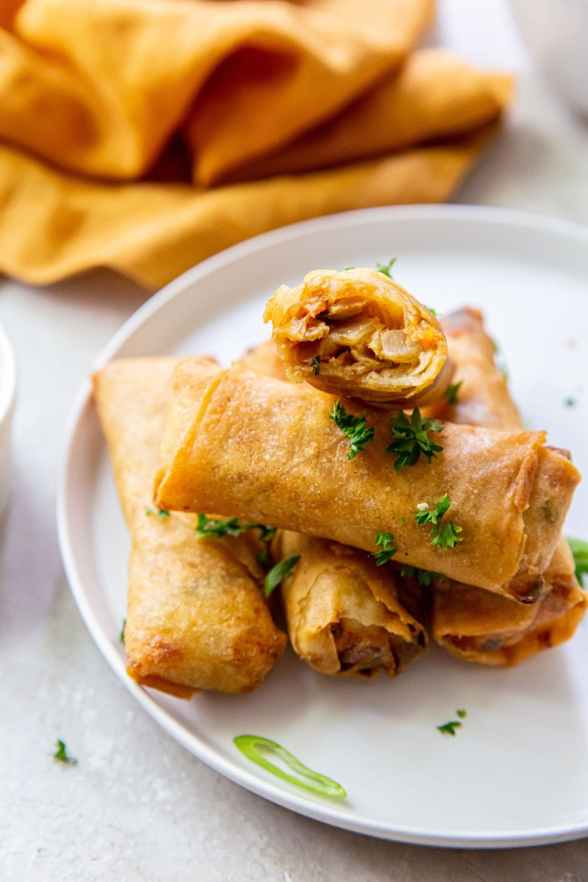 white plate with spring rolls on it. orange bowl next to it.