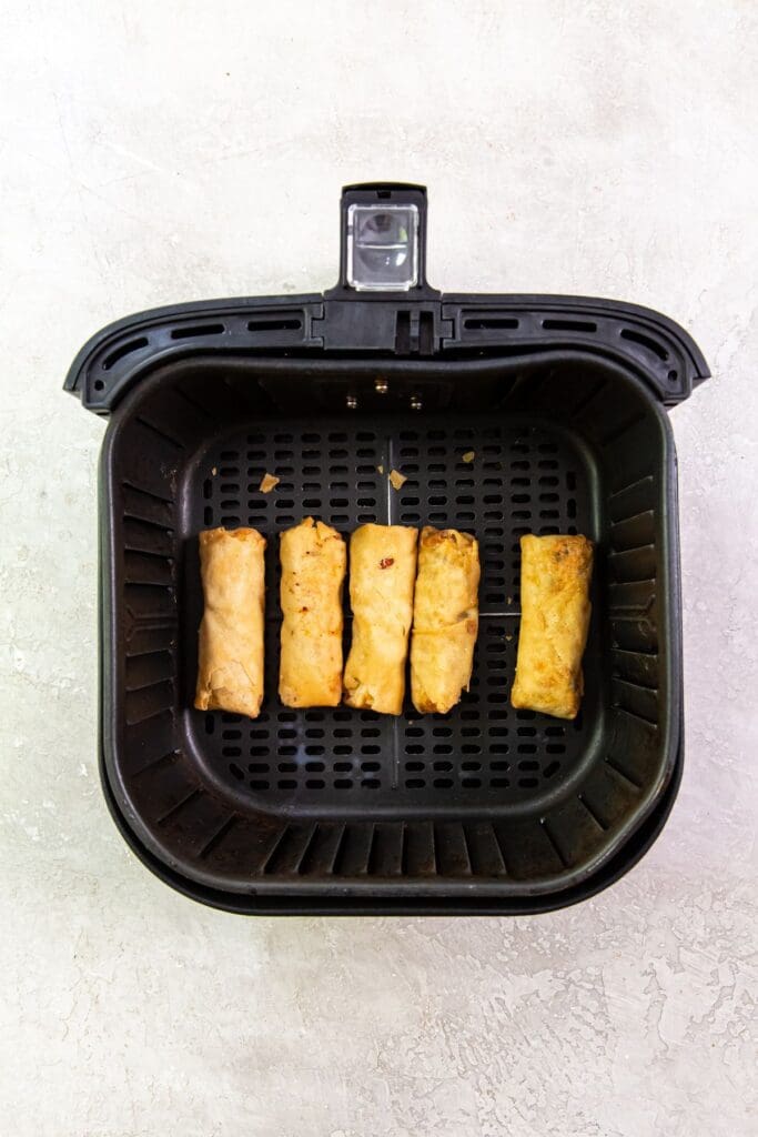 black air fryer basket with frozen chicken inside.