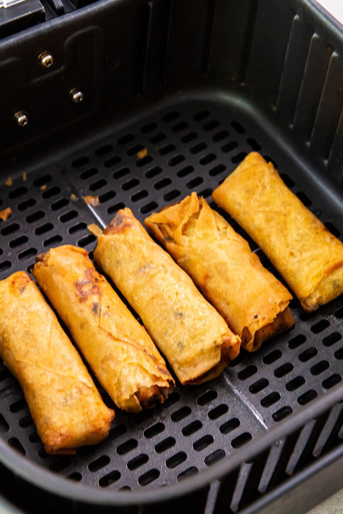 black air fryer basket with cooked chicken inside.