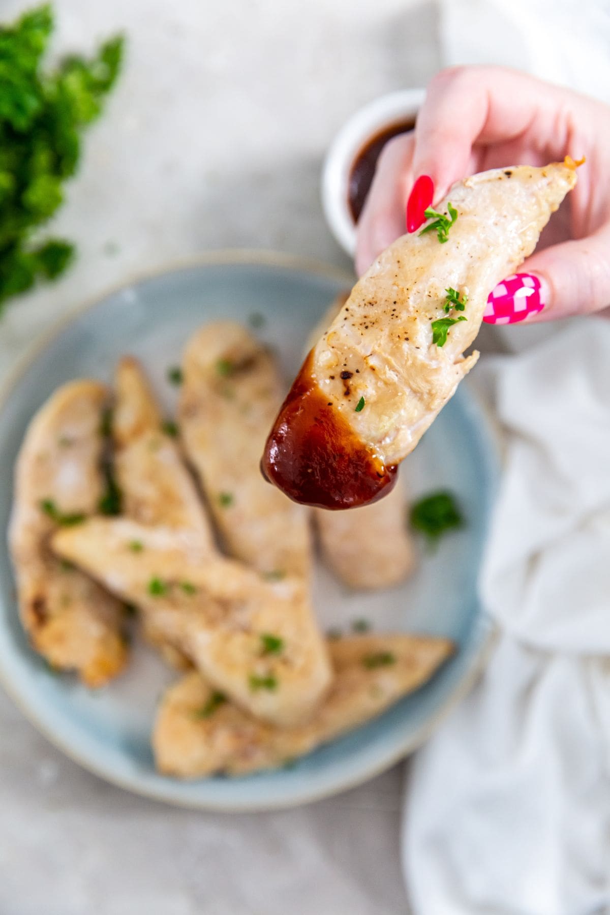 A Person holding one tenders up with bbq sauce on it.