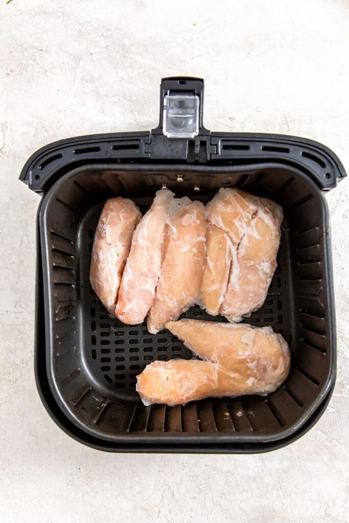 black air fryer basket with raw chicken inside.