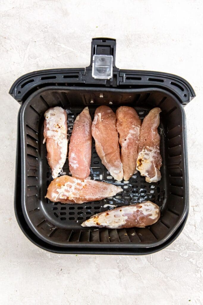 black air fryer basket with raw chicken inside.