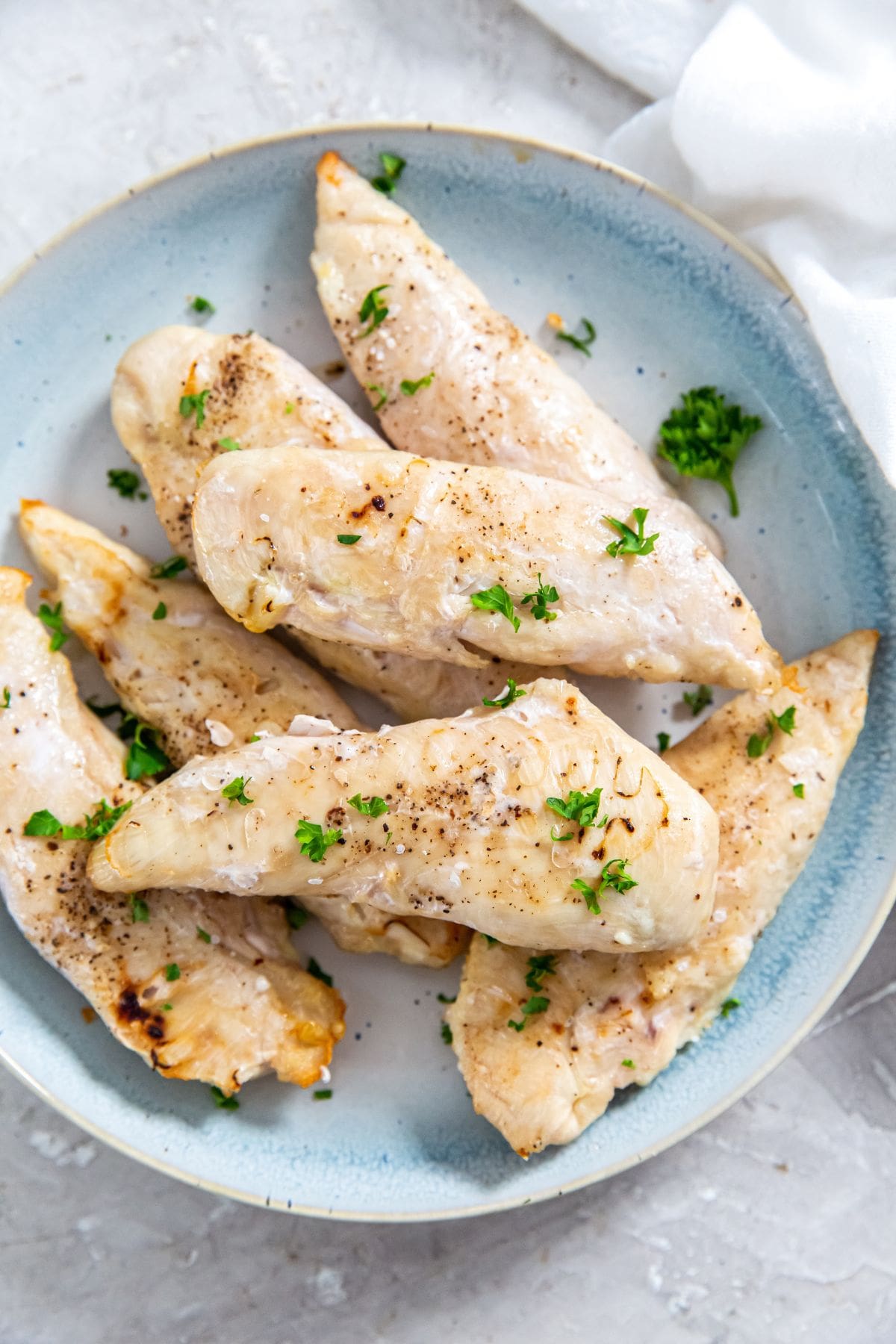 air fryer frozen chicken tenders on a blue plate with parsley on top. white towel next to it.