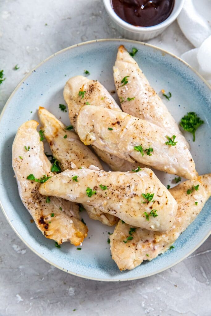 air fryer frozen chicken tenders on a blue plate with parsley on top. white towel next to it. BBQ sauce in the back.