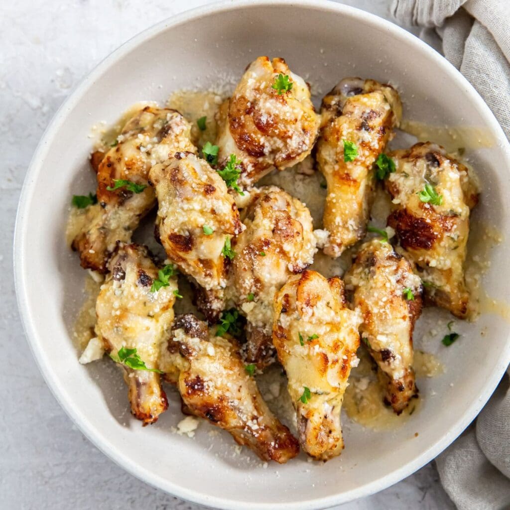 garlic Parmesan wings in white bowl. gray towel next to it.