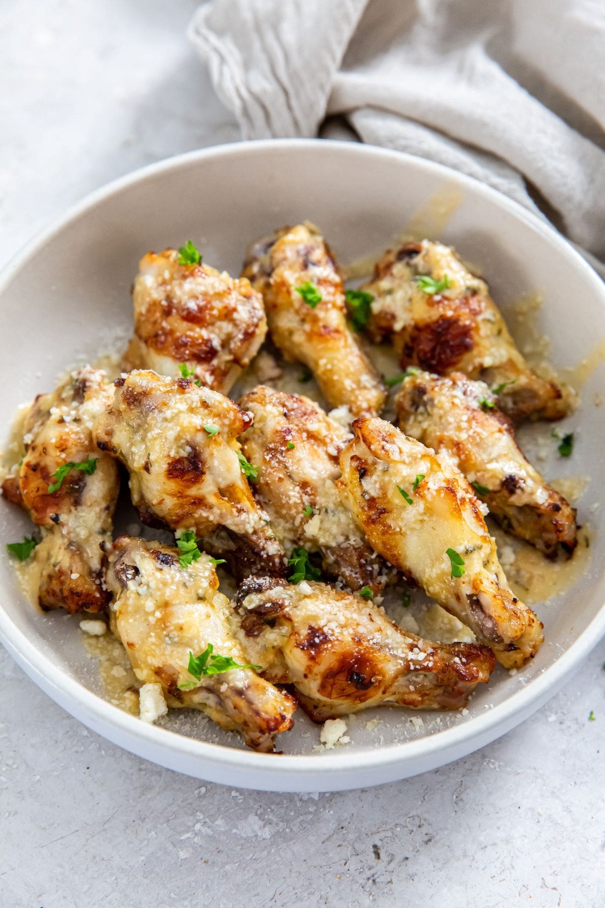 garlic Parmesan wings in white bowl. gray towel next to it.