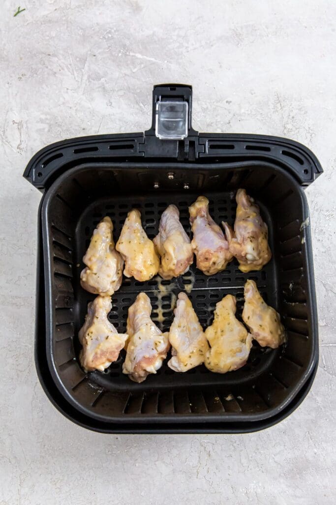 black air fryer basket with raw chicken wings inside