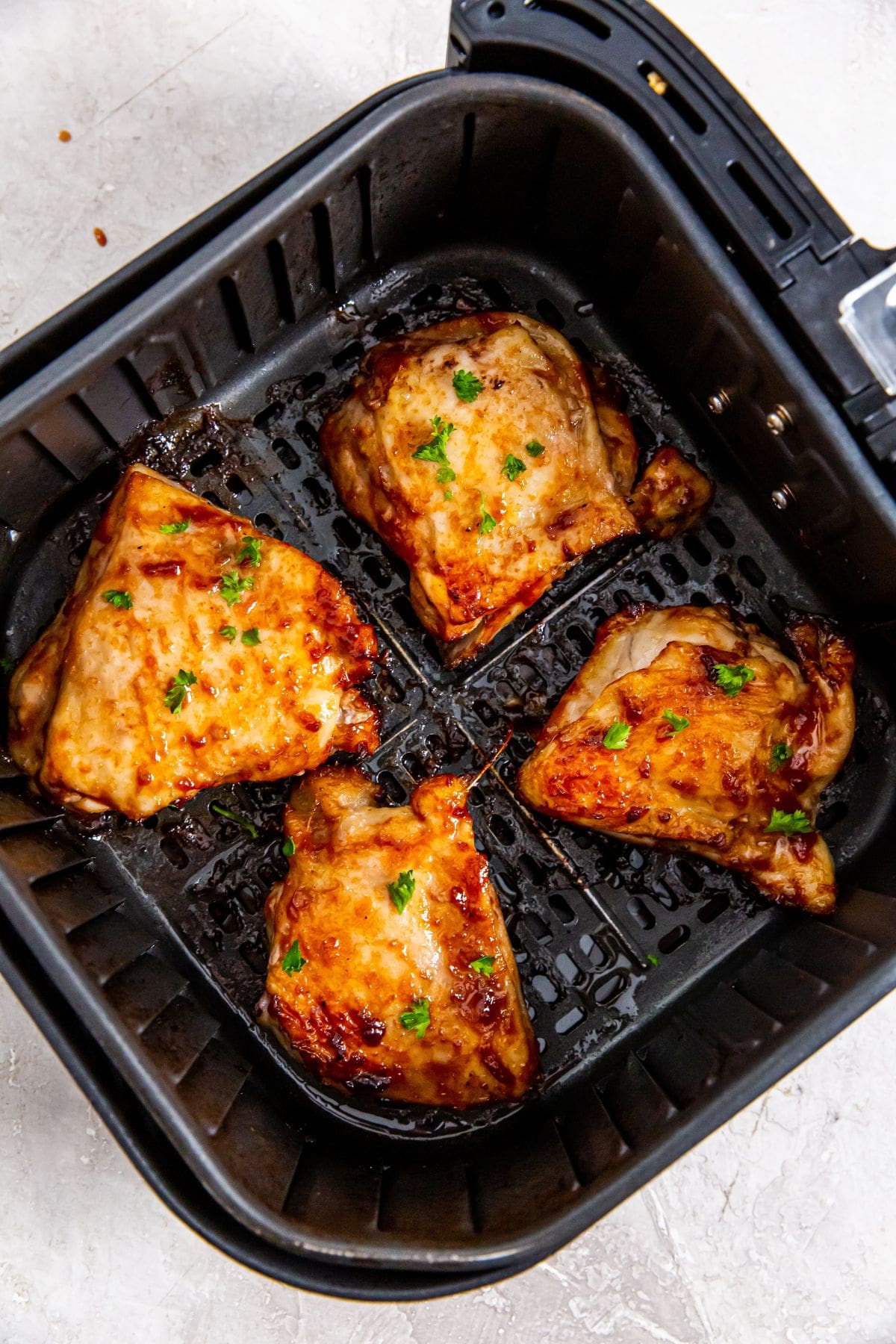 Black air fryer basket with cooked bbq chicken thighs inside