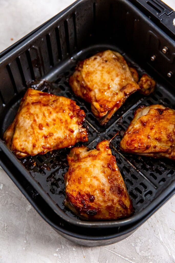 Black air fryer basket with cooked bbq chicken thighs inside