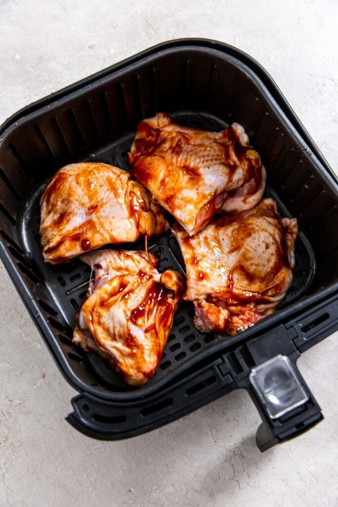 Black air fryer basket with raw bbq chicken thighs inside