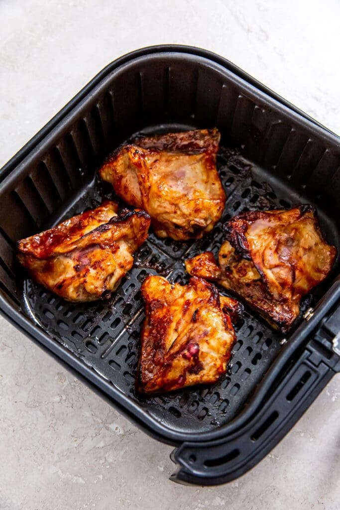 Black air fryer basket with cooked bbq chicken thighs inside