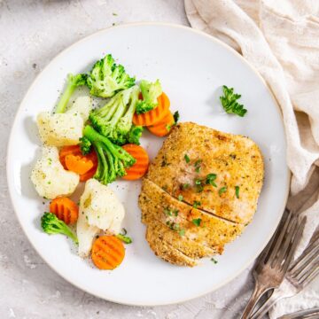 white plate with chicken and vegetables. Silverware and towels next to it.