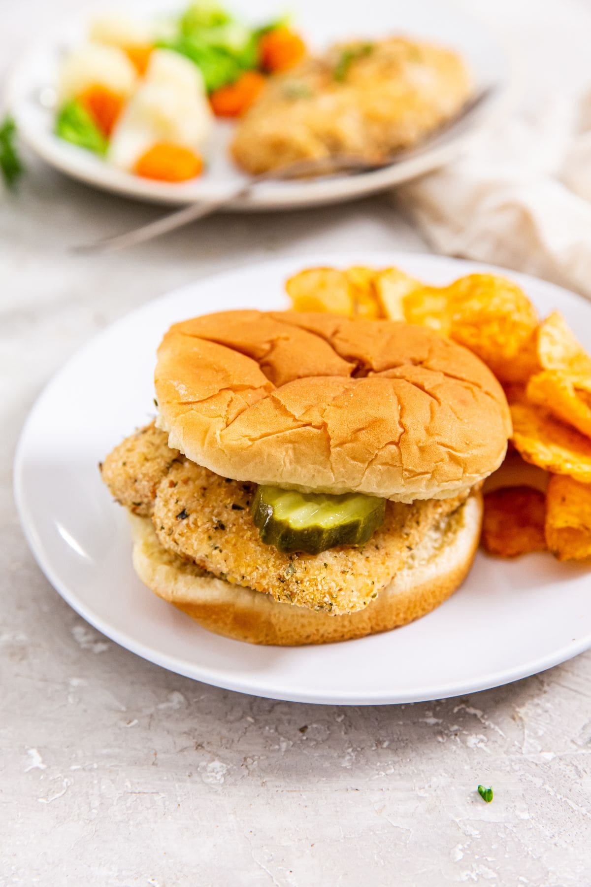 white plate with chicken sandwich and chips on it.