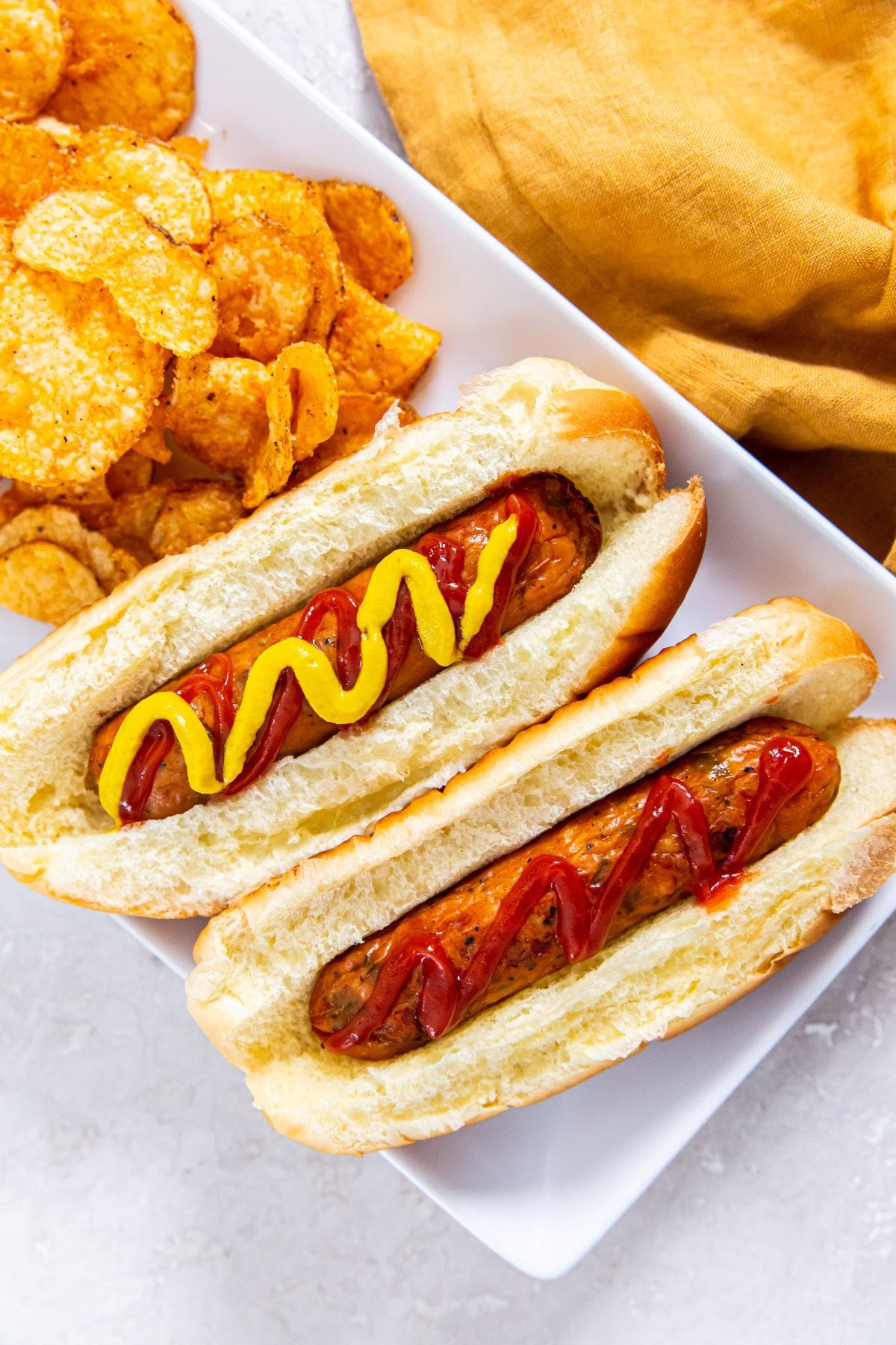 chicken sausages topped with ketchup and served alongside crispy potato chips.