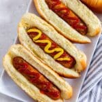 Four air-fried chicken sausages on a plate with mustard and ketchup.