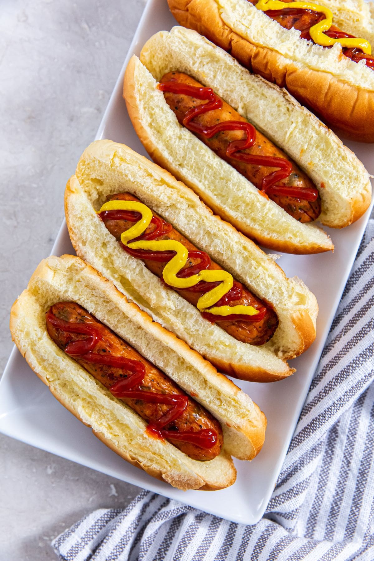 Four air-fried chicken sausages on a plate with mustard and ketchup.