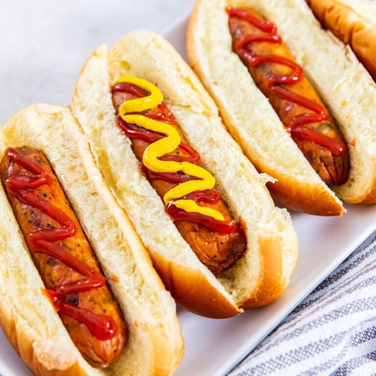 Four chicken sausages cooked in an air fryer served with ketchup and mustard on a plate.