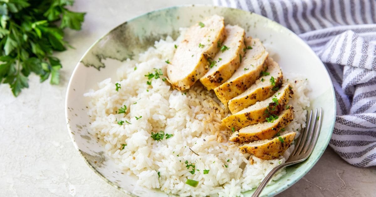 Air Fryer Lemon Pepper Chicken Breast on a white and teal plate with parsley, rice and a fork.