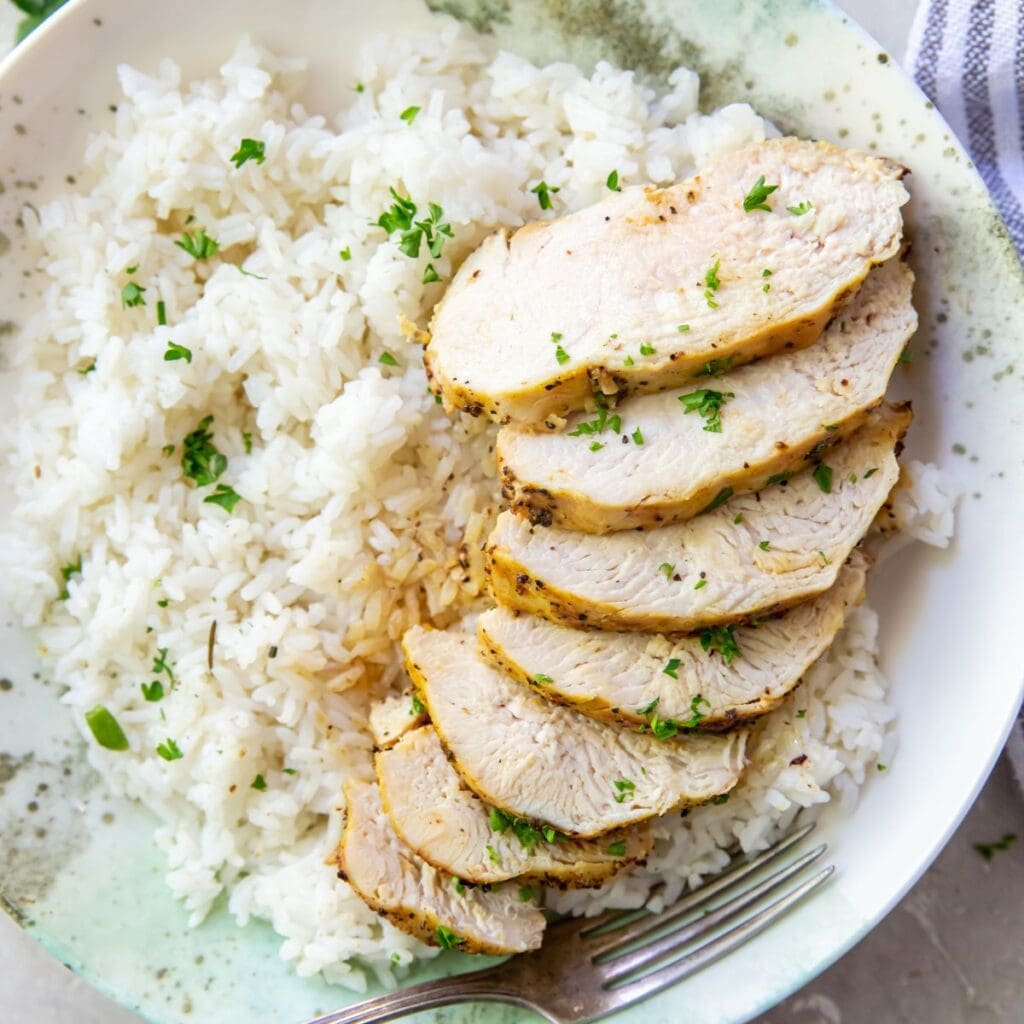 Grilled chicken breasts with lemon pepper seasoning served on a plate with rice and herbs.