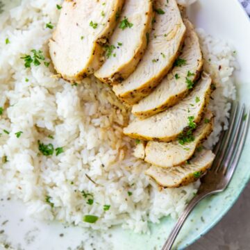 Sliced air fryer chicken breast with lemon pepper on a plate with rice and parsley.