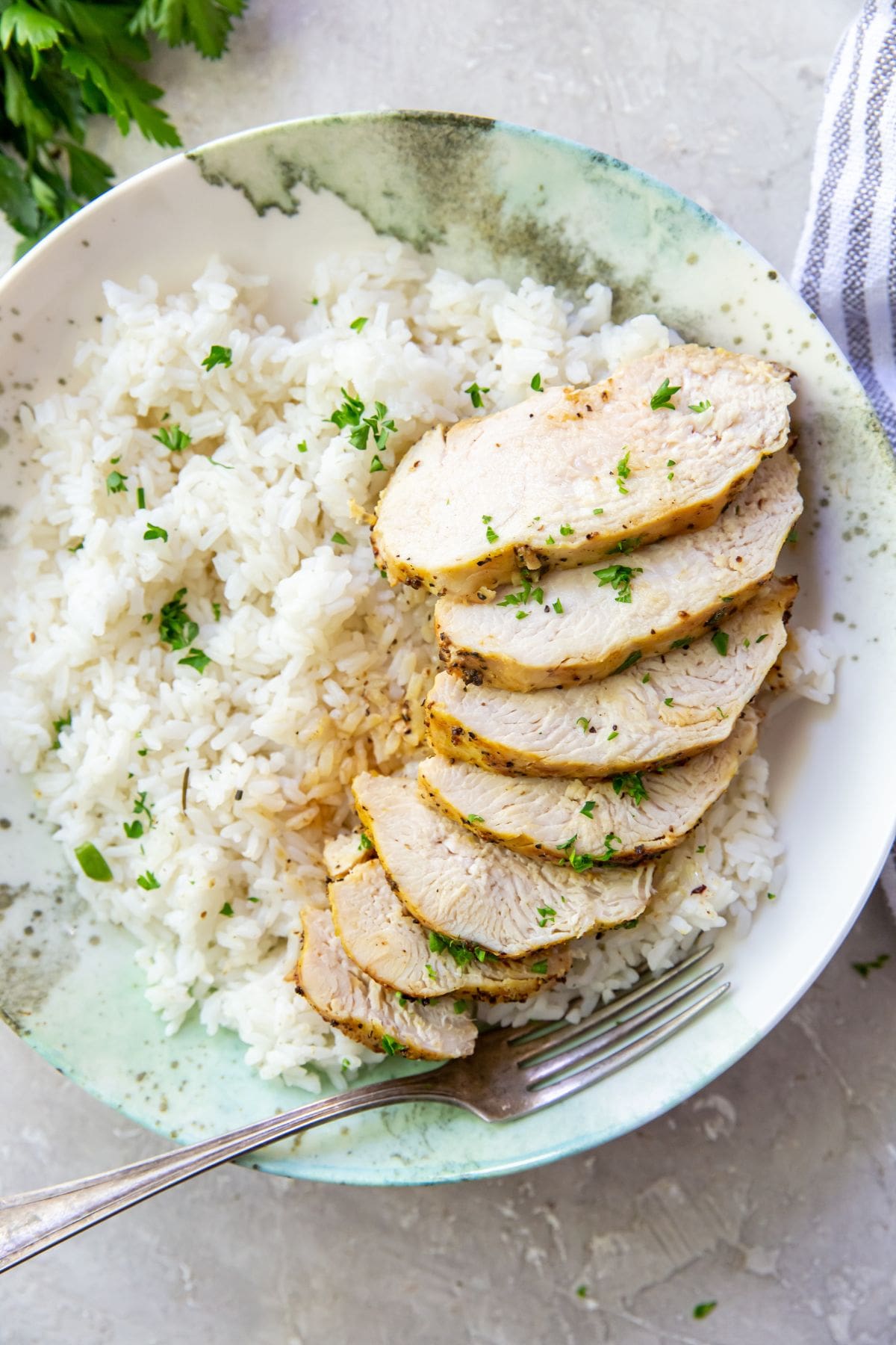 Sliced lemon pepper chicken breasts served with rice and parsley.