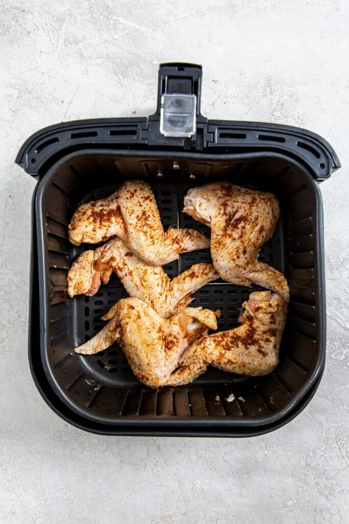 black air fryer basket with raw whole chicken wings inside.