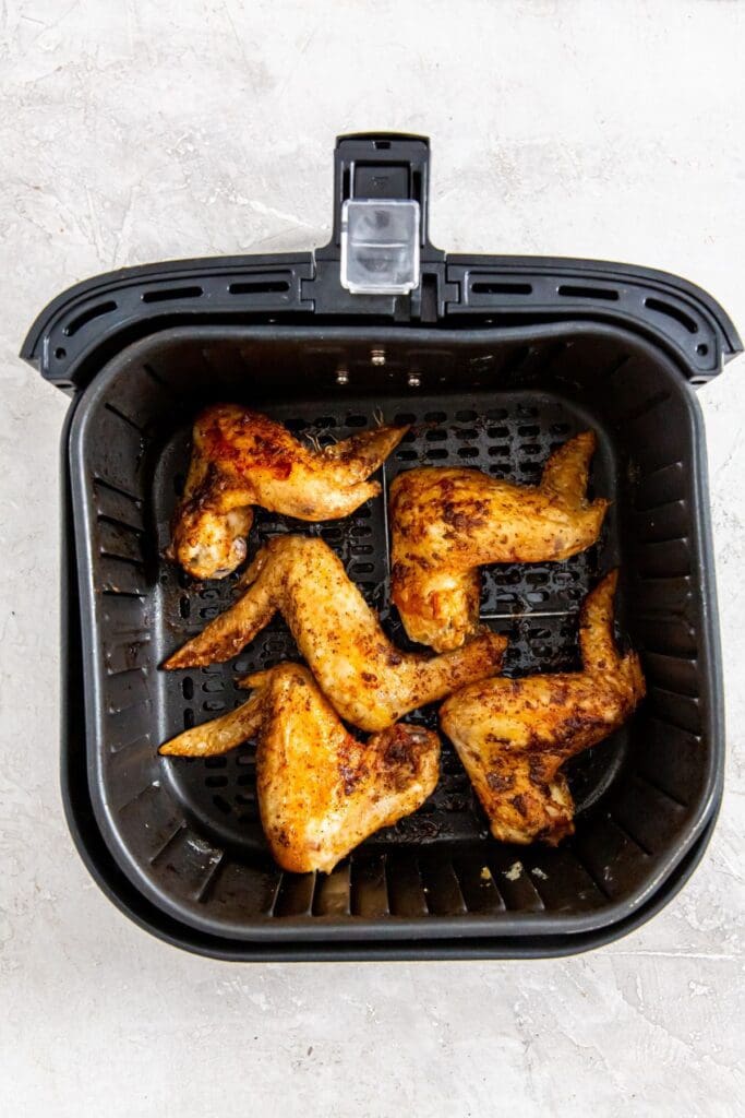 black air fryer basket with cooked whole chicken wings inside