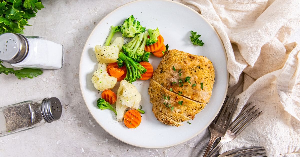 Air Fryer Chicken Cutlets on a white plate with parsley, carrots, broccoli, and cauliflower.