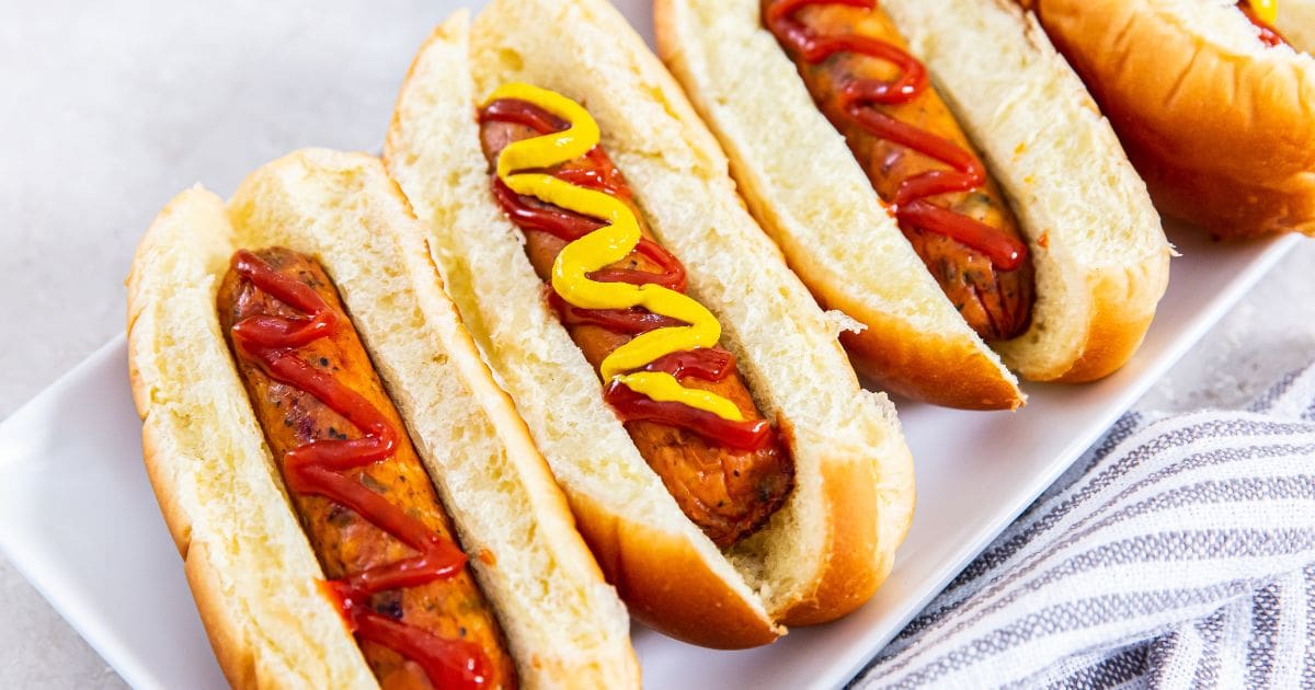 Four chicken sausages cooked perfectly in an air fryer, served with ketchup and mustard on a plate.