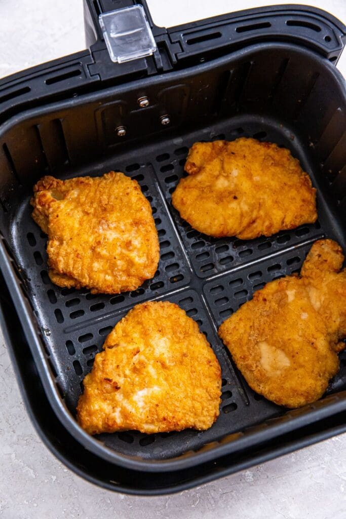 Black air fryer basket with cooked chicken breast fillets inside