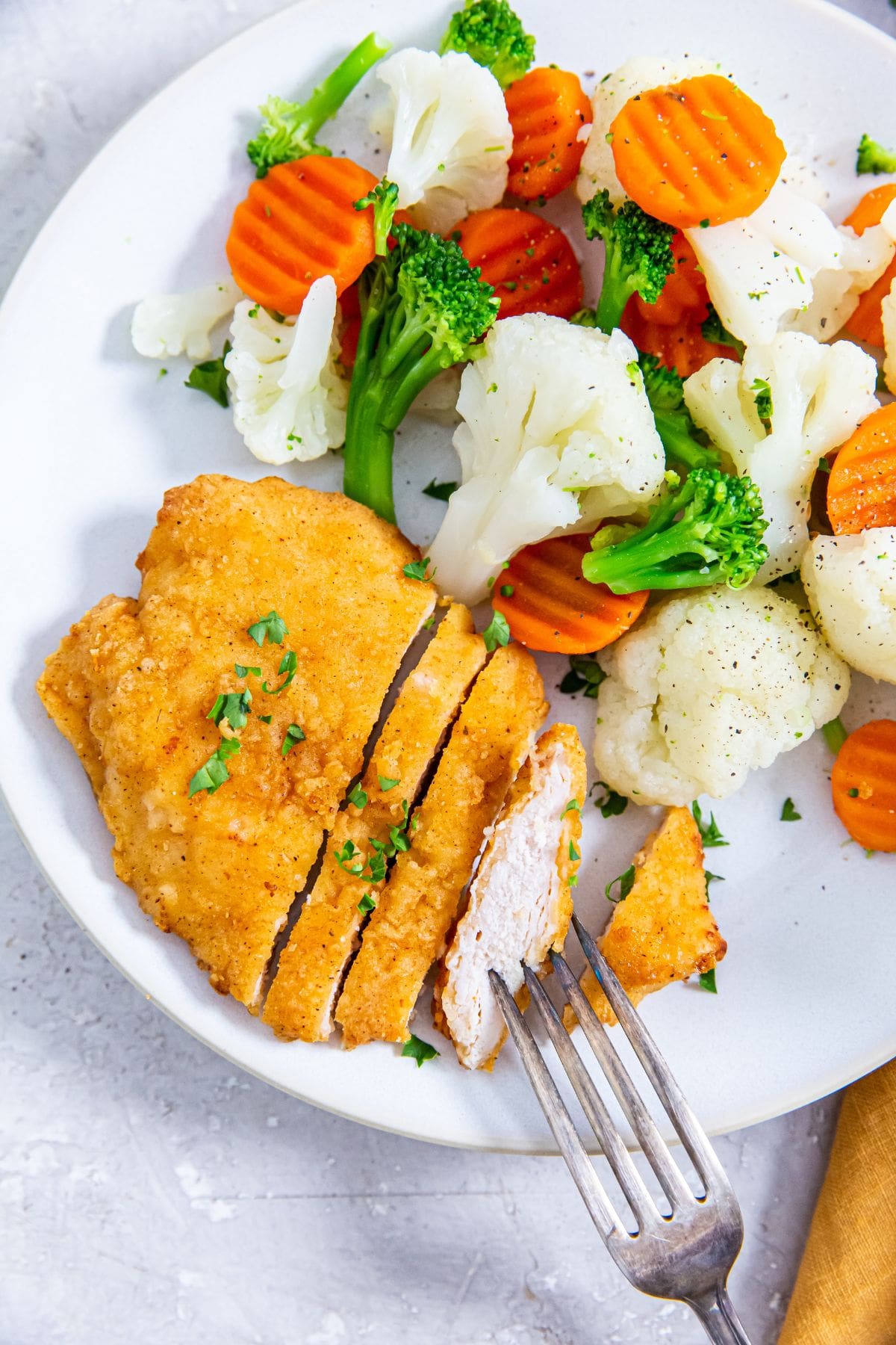 Aldi's Red Bag Chicken breast on a plate with vegetables and a fork.