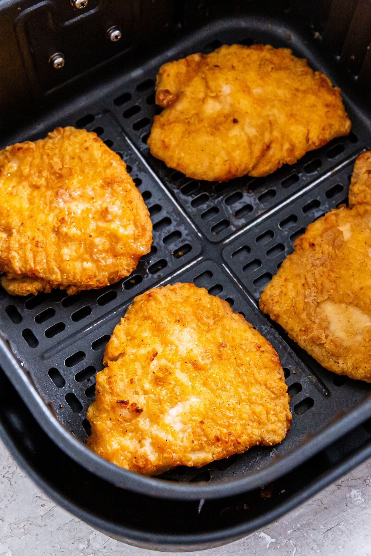 Black air fryer basket with cooked chicken breast fillets inside 