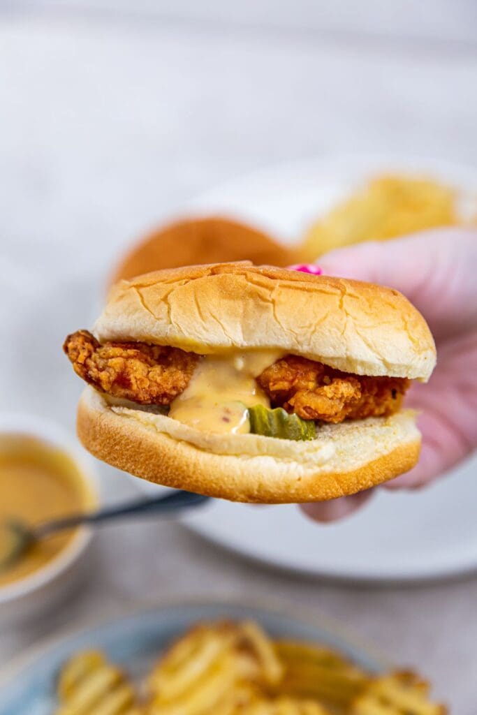 A person holding a chicken sandwich with fries on a plate.