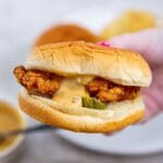 A person holding a sandwich with fries on a plate.