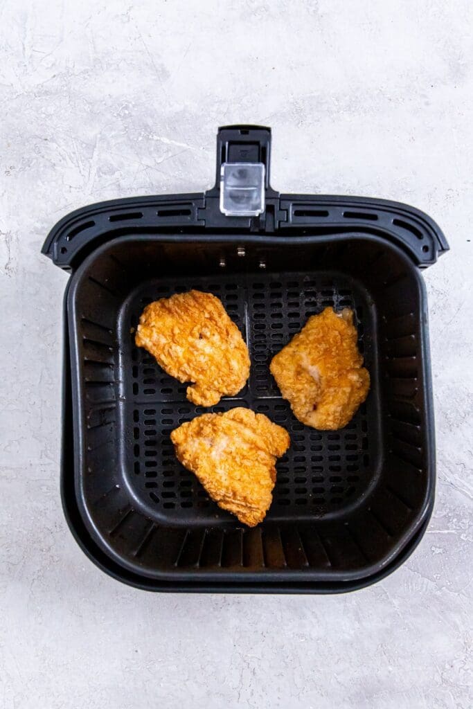 raw chicken patties inside a black air fryer basket.