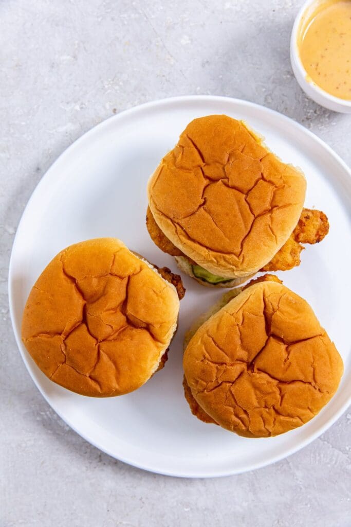 Three chicken sandwiches on a plate with dipping sauce.