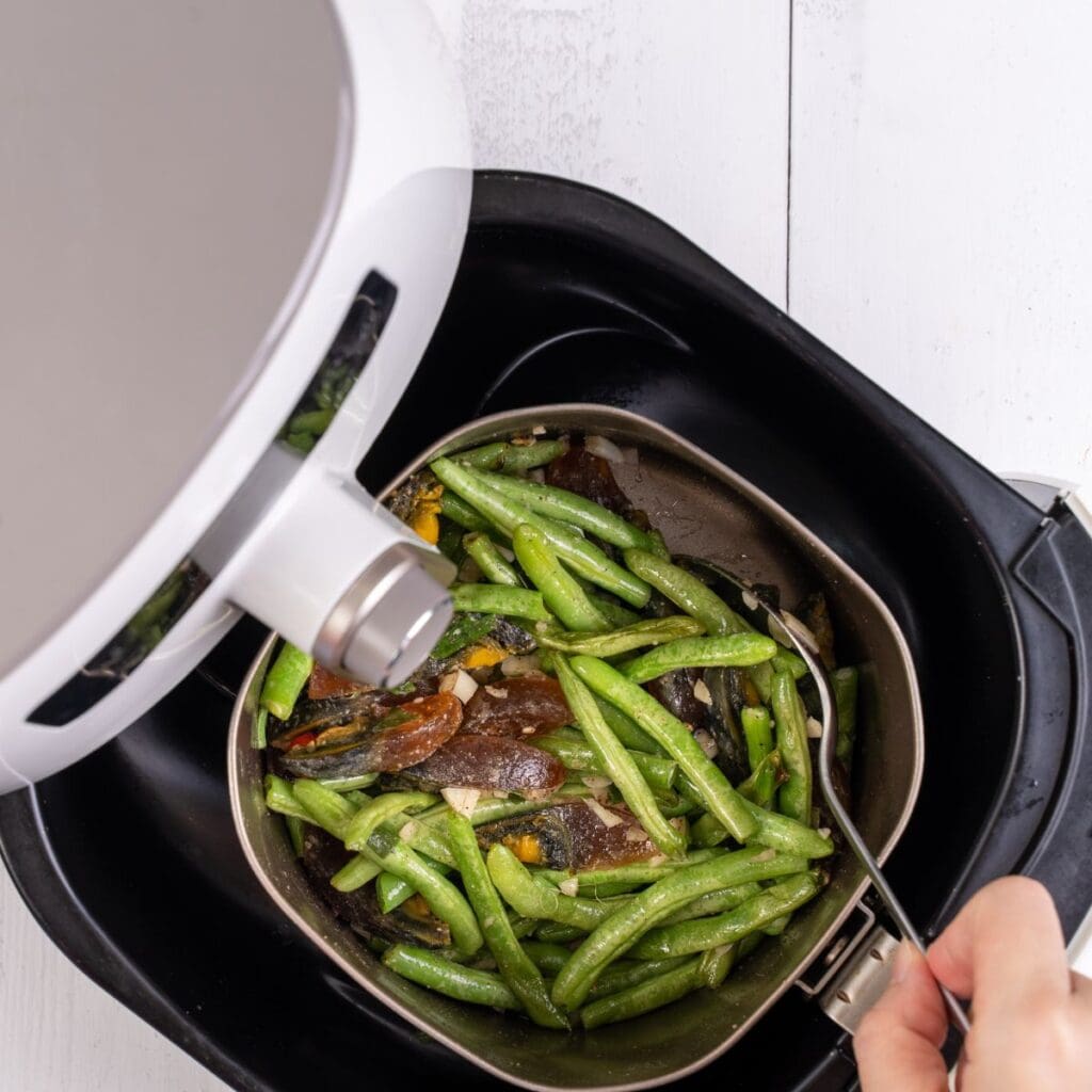 An air fryer filled with green beans and mushrooms, accessorized with air fryer accessories.