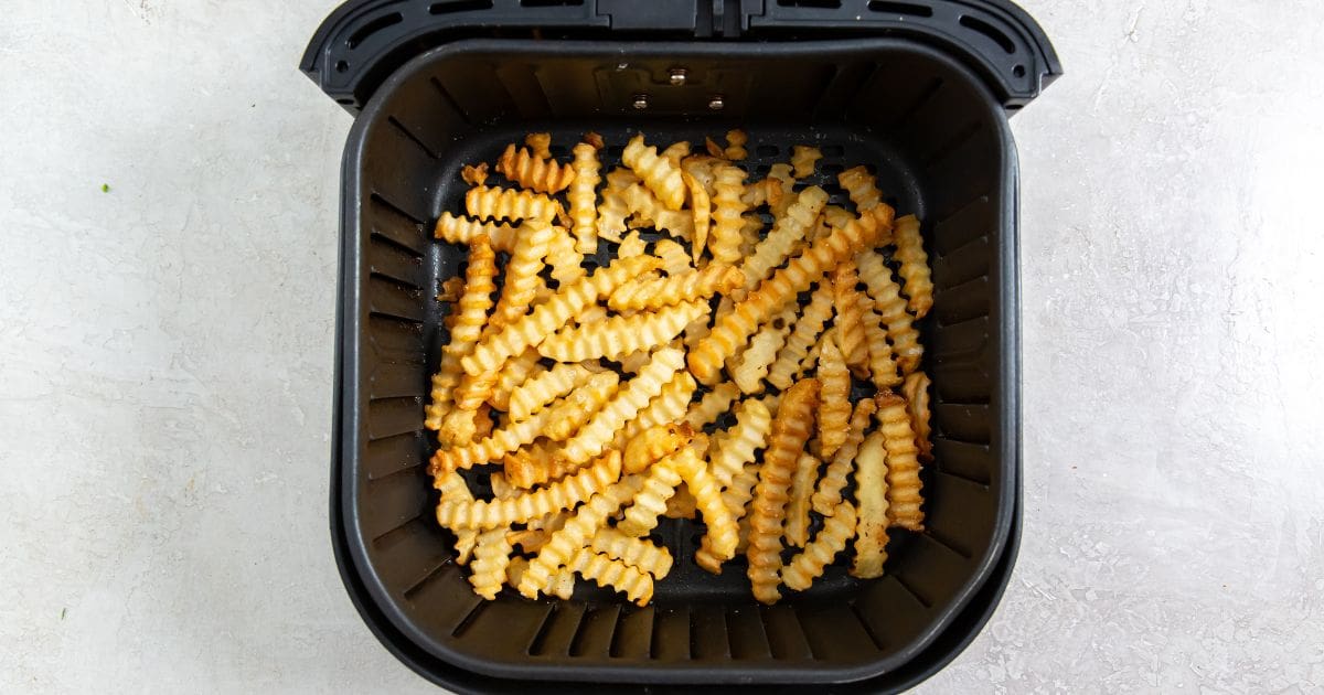 Black air fryer basket with cooked fries inside.