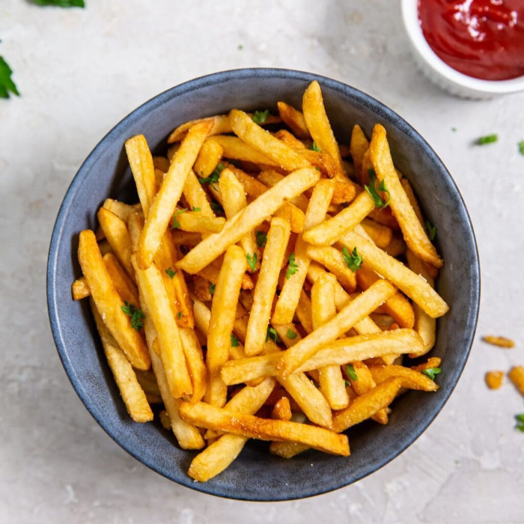 Frozen French fries cooked in an air fryer, served in a bowl with ketchup.