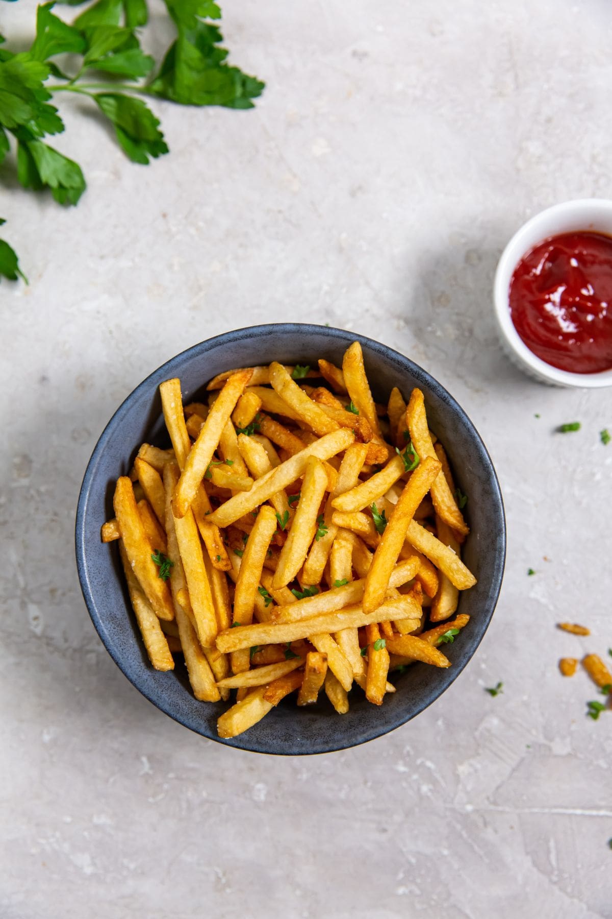 French fries cooked in an air fryer, served in a bowl with ketchup and parsley.