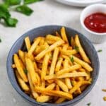 fries cooked in an air fryer and served in a bowl with ketchup.