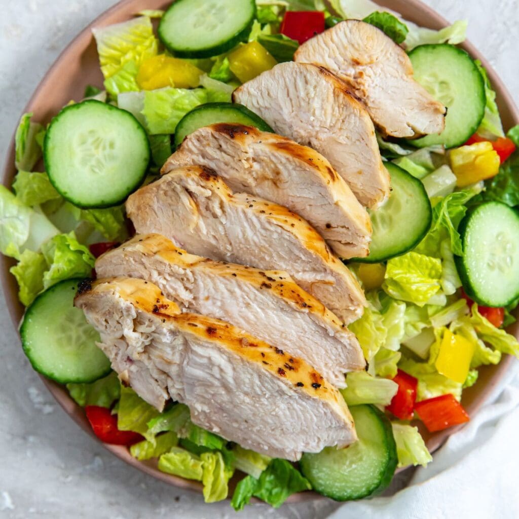 Grilled chicken salad on a plate with air-fried Italian chicken breast, cucumbers, and tomatoes.