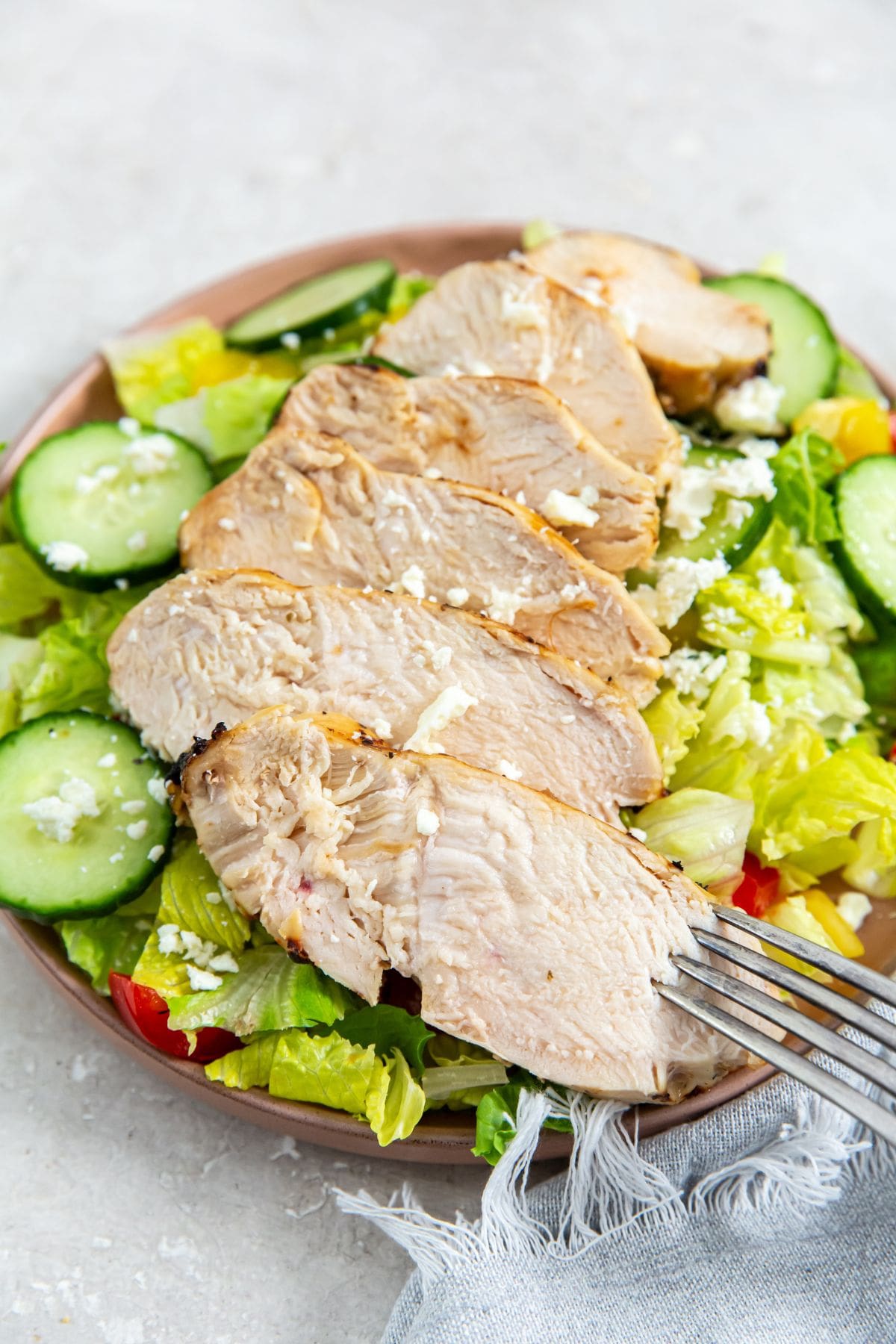 chicken on the top of a salad with cucumbers and tomatoes on a plate.