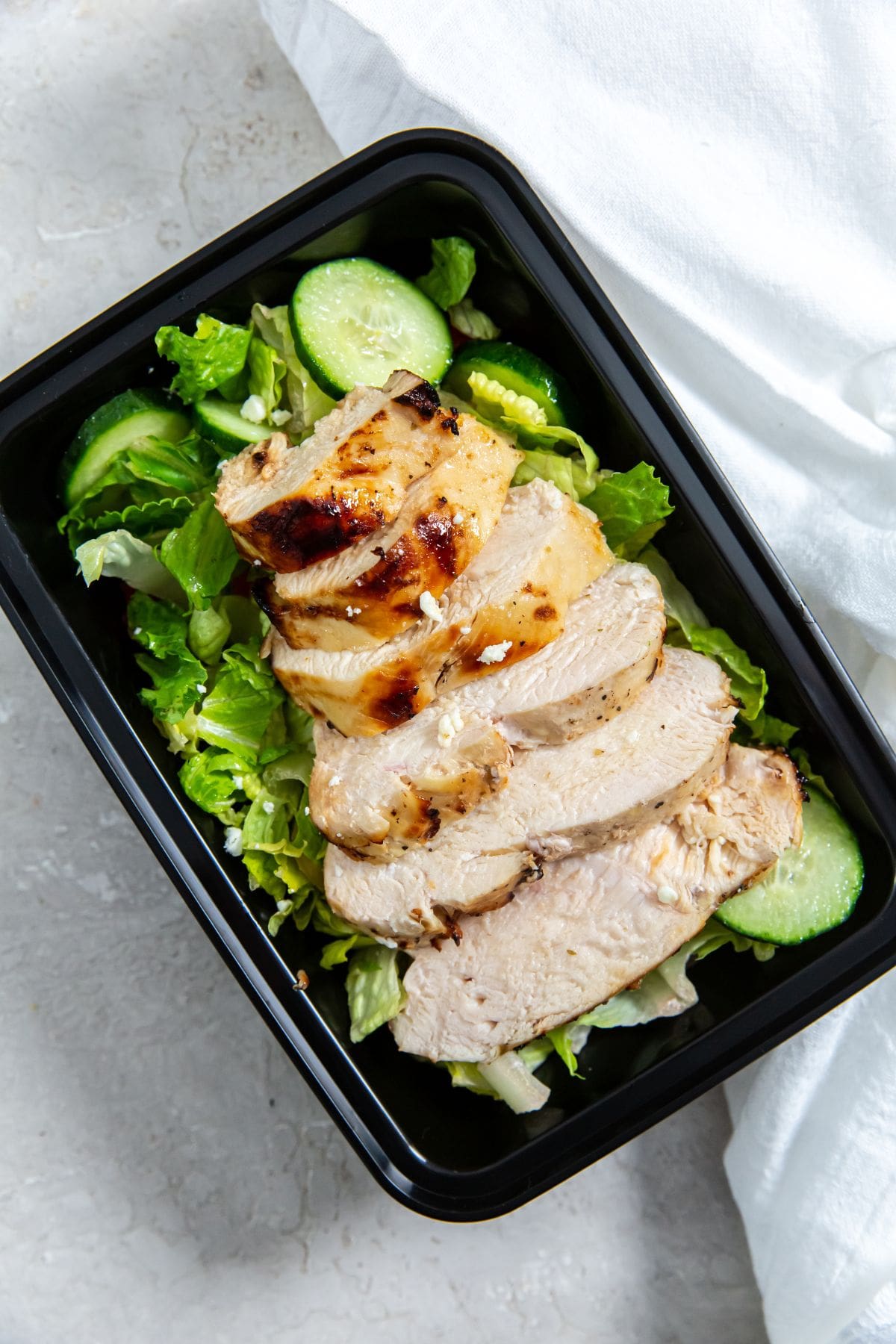 chicken on the top of a salad with cucumbers and tomatoes on a plate.