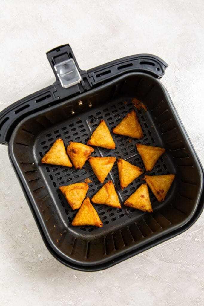 Black air fryer basket with cooked tikka samosas