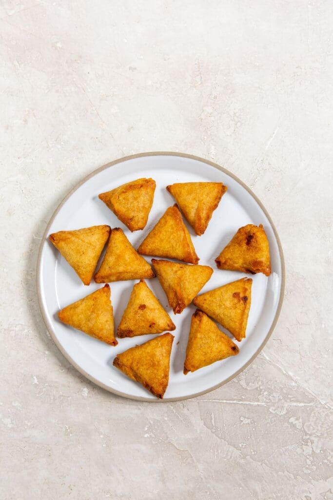 A plate full of mini chicken tikka samosas, on a white surface.