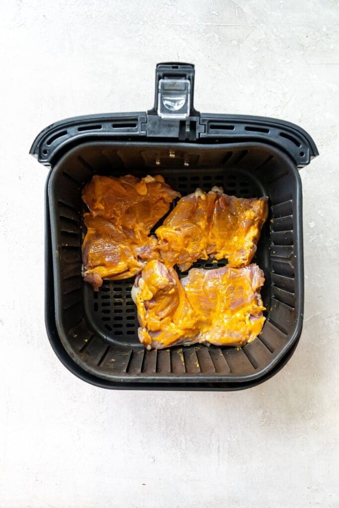 Black air fryer basket with raw chicken inside