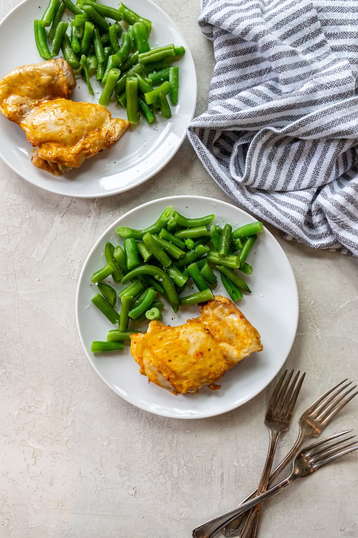 white plate with chicken and green beans on it. fork next to chicken. striped towel next to plates.